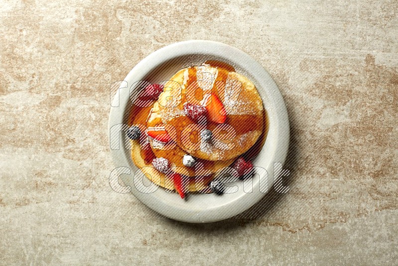 Three stacked mixed berries pancakes in a grey plate on beige background