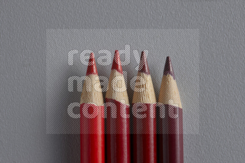 A collection of sharpened colored pencils arranged showcasing a gradient of red hues on grey background