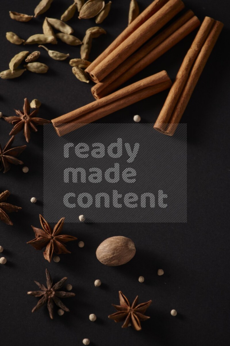 أعواد من القرفة وحبوب الهيل واليانسون النجمي وجوزة الطيب وحبوب الفلفل الأبيض علي خلفية سوداء