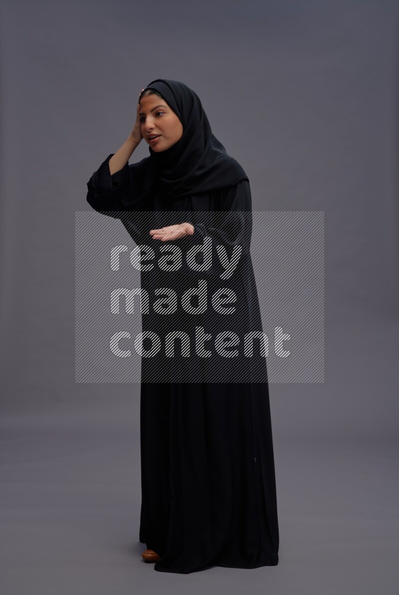 Saudi woman wearing Abaya standing interacting with the camera on gray background