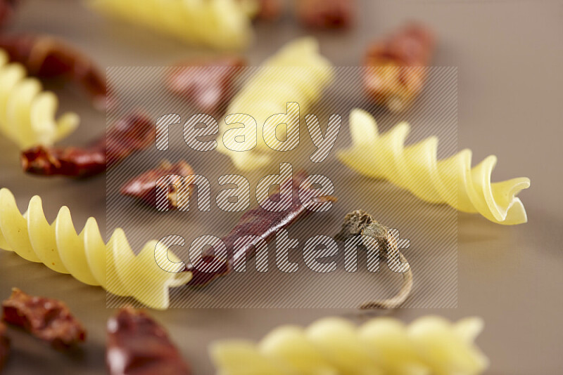 Raw pasta with different ingredients such as cherry tomatoes, garlic, onions, red chilis, black pepper, white pepper, bay laurel leaves, rosemary and cardamom on beige background