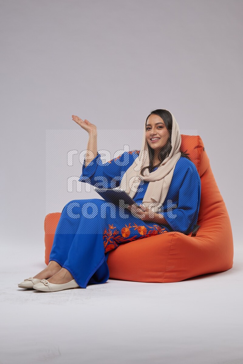 A Saudi woman sitting on an orange beanbag and working on tablet