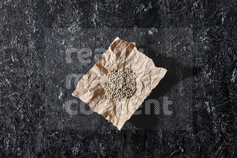 White pepper beads in a crumpled piece of on textured black flooring