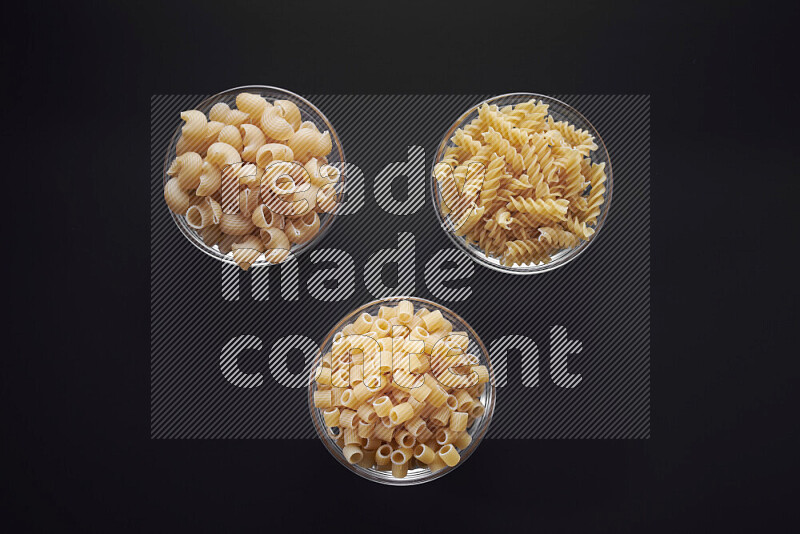 Different pasta types in glass bowls on black background