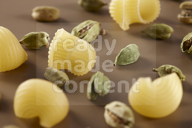 Raw pasta with different ingredients such as cherry tomatoes, garlic, onions, red chilis, black pepper, white pepper, bay laurel leaves, rosemary and cardamom on beige background