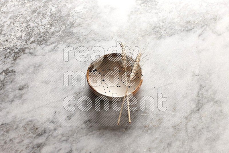 Wheat stalks on Multicolored Pottery Bowl on grey marble flooring, 45 degree angle