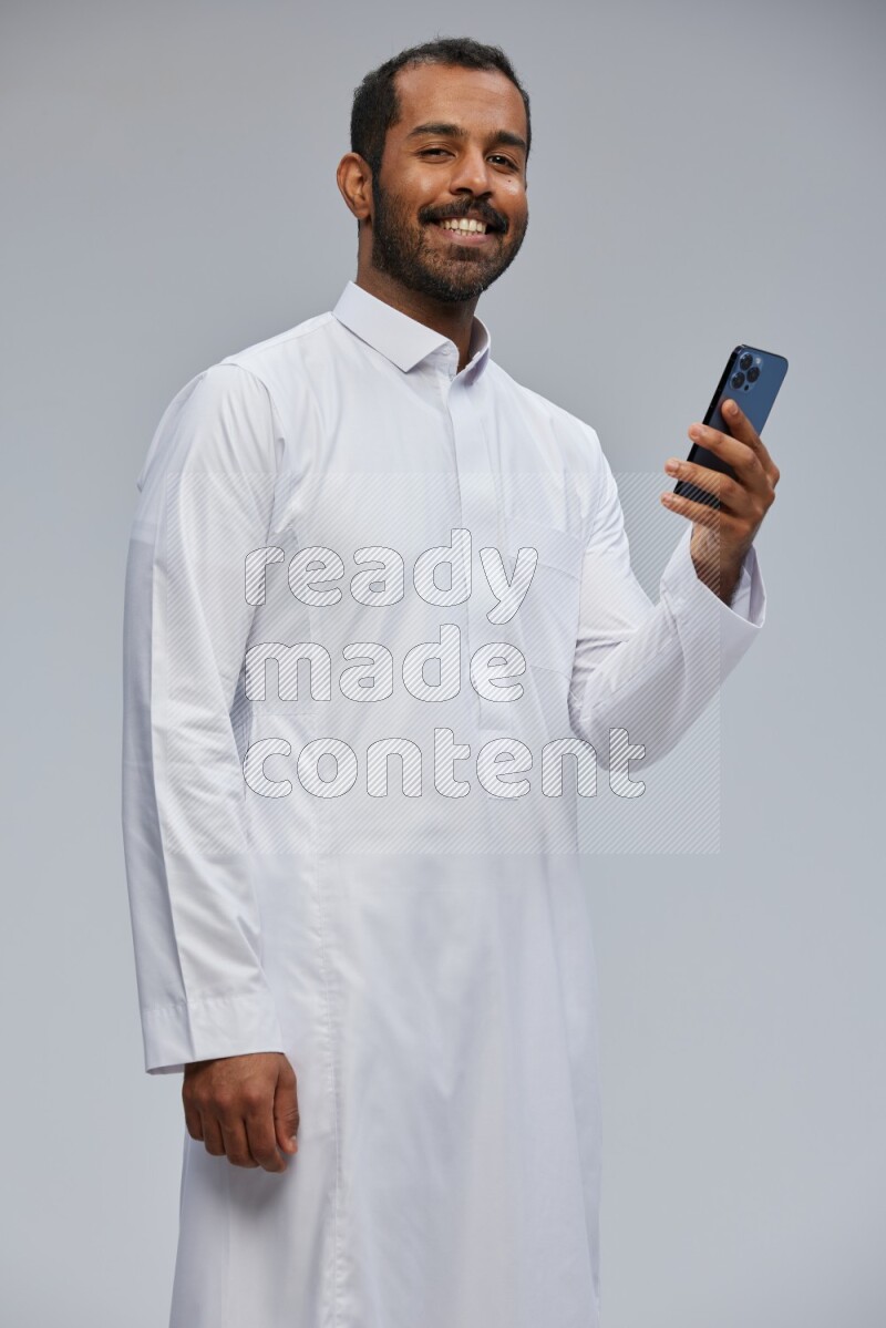 Saudi man wearing Thob standing texting on phone on Gray background