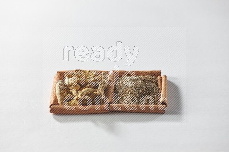 مربعان من أعواد القرفة ممتلئان بحبوب الكمون وأصابع الكركم علي خلفية بيضاء