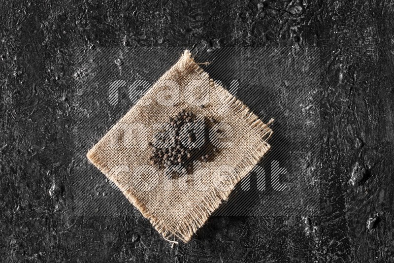 Black pepper on burlap fabric on a textured black flooring