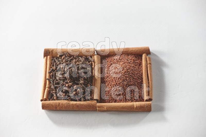 مربعان من أعواد القرفة ممتلئان بحب الرشاد والقرنفل علي خلفية بيضاء