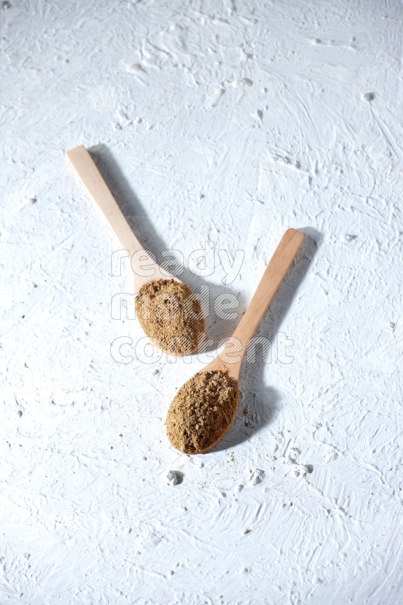 Wooden spoons full of allspice powder and allspice whole balls spreaded on a textured white flooring