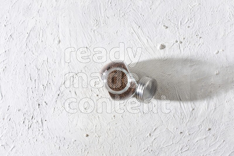 A glass spice jar full of cloves powder on textured white flooring