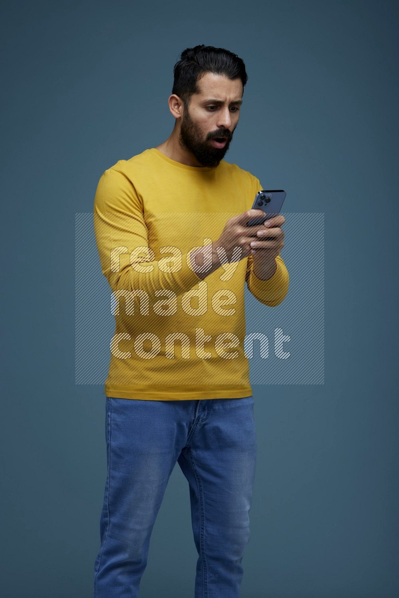 Man typing on his phone in a blue background wearing a yellow shirt