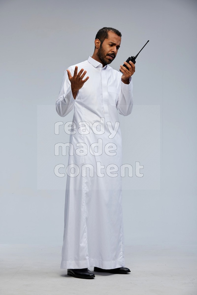 Saudi man Wearing thob standing holding walkie-talkie on Gray background