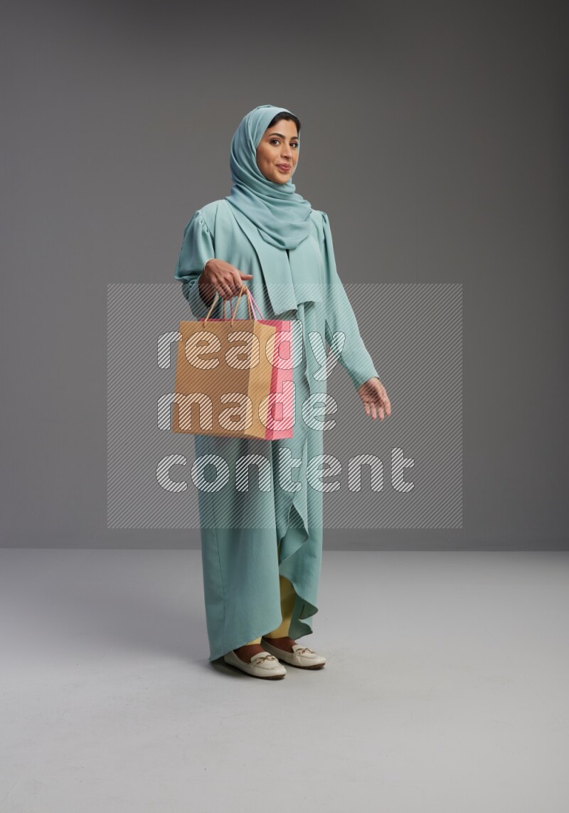 Saudi Woman wearing Abaya standing holding shopping bag on Gray background