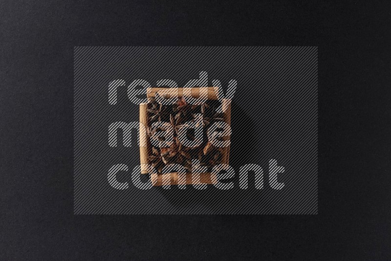 A single square of cinnamon sticks full of star anise on black flooring