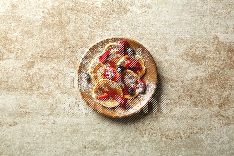 Five stacked mixed berries mini pancakes in a brown plate on beige background