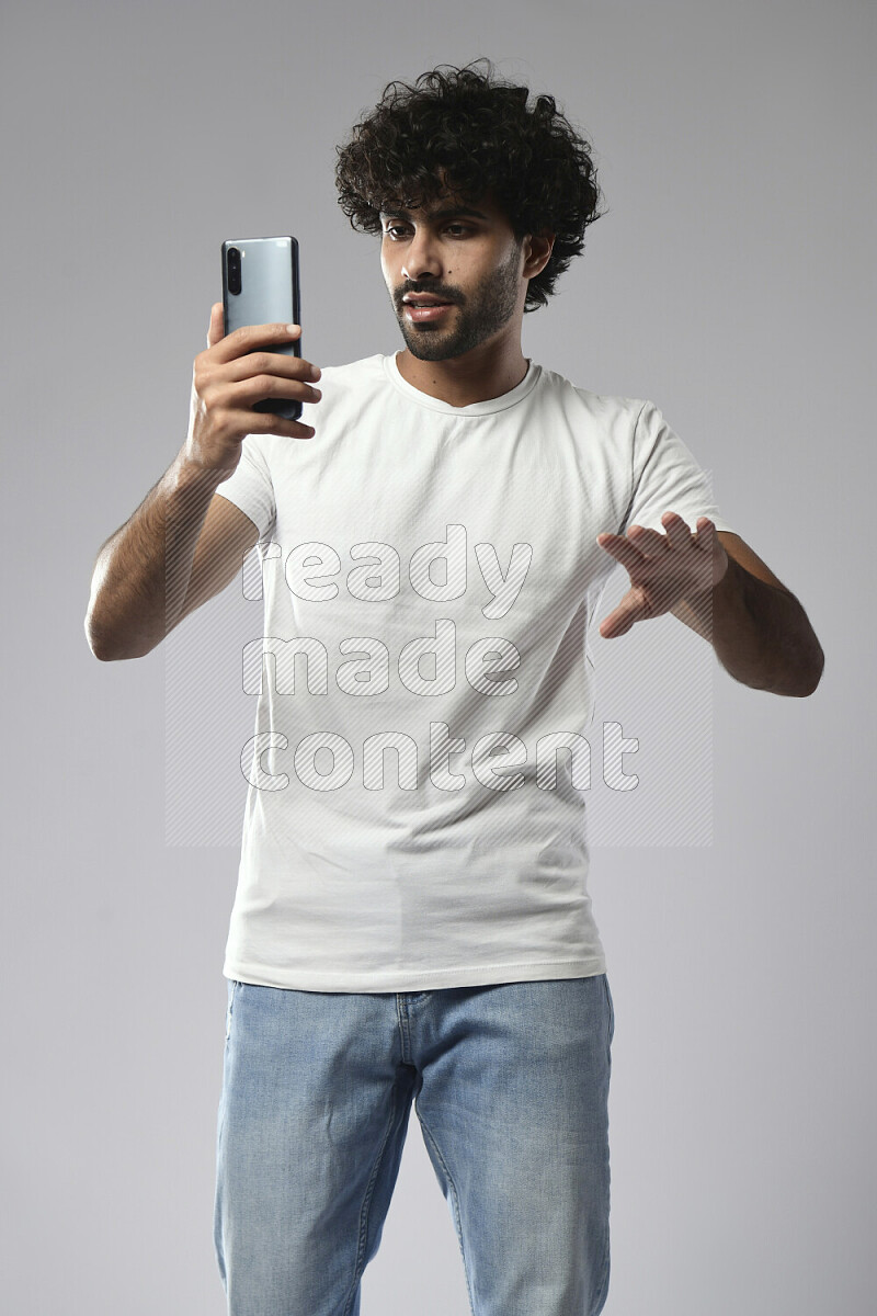 A man wearing casual standing and shooting with his phone on white background