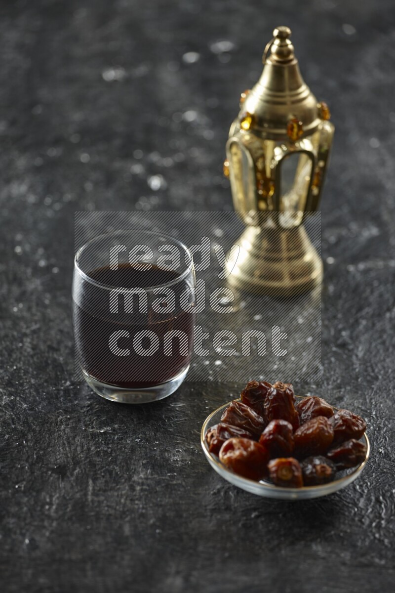 A golden lantern with different drinks, dates, nuts, prayer beads and quran on textured black background