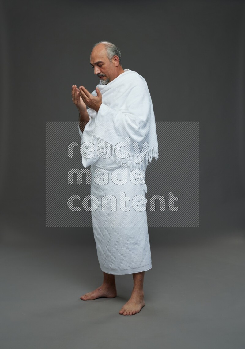 A man wearing Ehram Standing dua'a on gray background