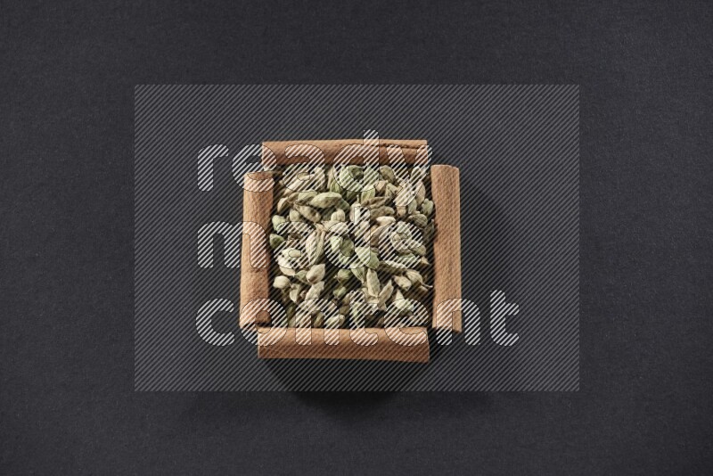 A single square of cinnamon sticks full of Cardamom on black flooring