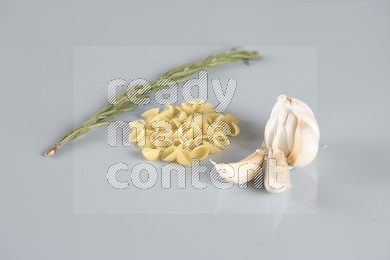 Raw pasta with different ingredients such as cherry tomatoes, garlic, onions, red chilis, black pepper, white pepper, bay laurel leaves, rosemary, cardamom and mushrooms on light blue background