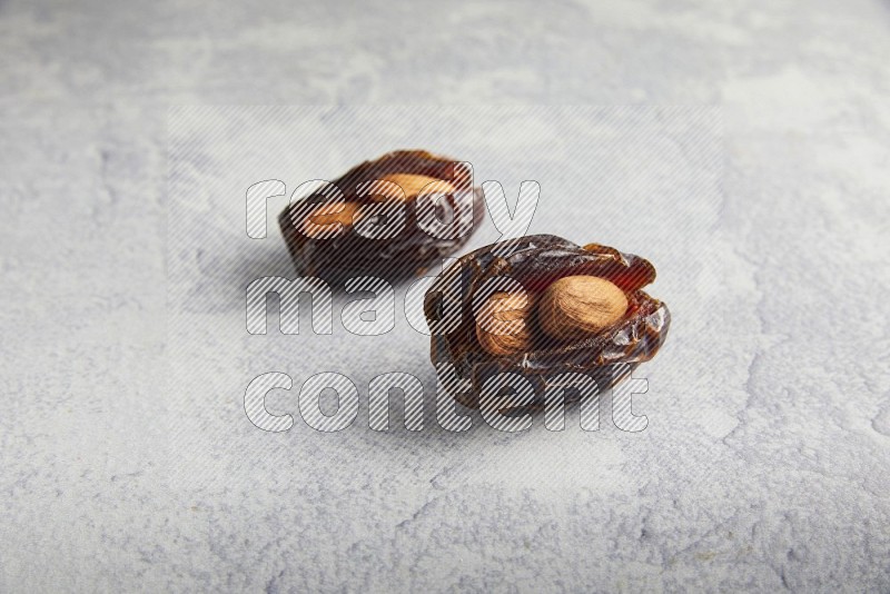 two almond stuffed madjoul dates on a light grey background