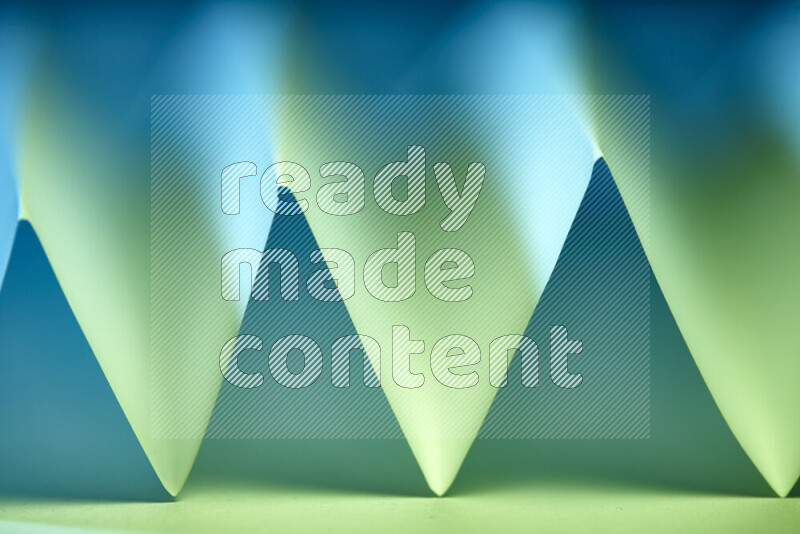 A close-up abstract image showing sharp geometric paper folds in green and blue gradients
