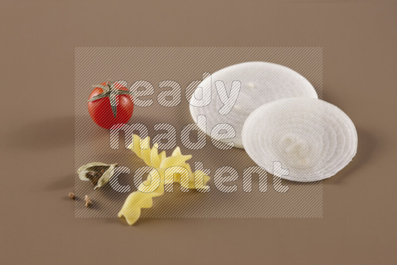 Raw pasta with different ingredients such as cherry tomatoes, garlic, onions, red chilis, black pepper, white pepper, bay laurel leaves, rosemary and cardamom on beige background