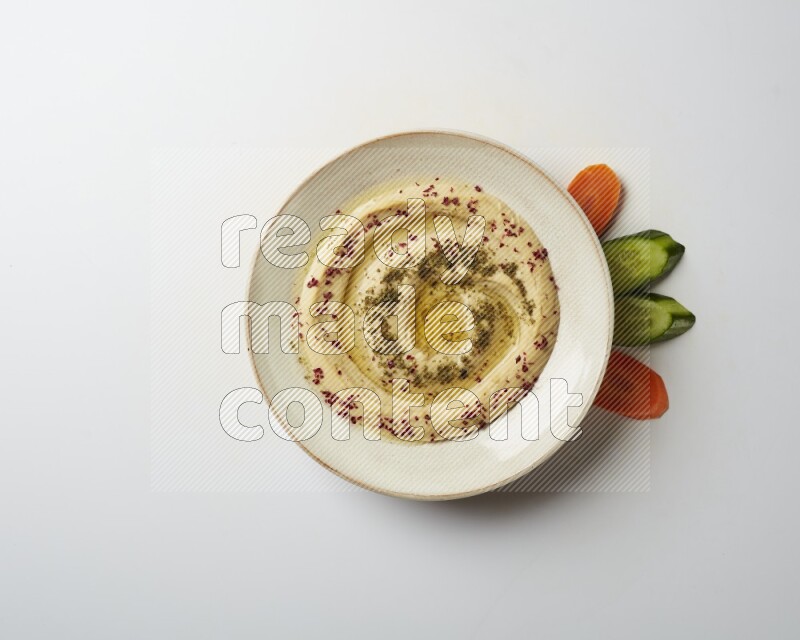 Hummus in a pottry plate garnished with zaatr & sumak on a white background