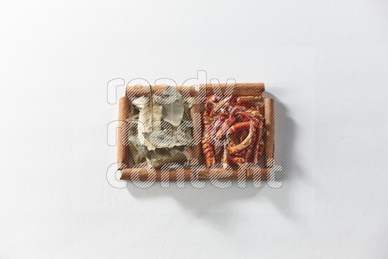 مربعان من أعواد القرفة ممتلئان بالفلفل الحار المجفف وأوراق الغار علي خلفية بيضاء