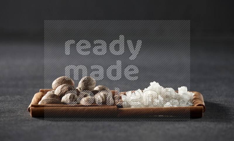 مربعان من أعواد القرفة ممتلئان بجوزة الطيب والملح الأبيض علي خلفية سوداء