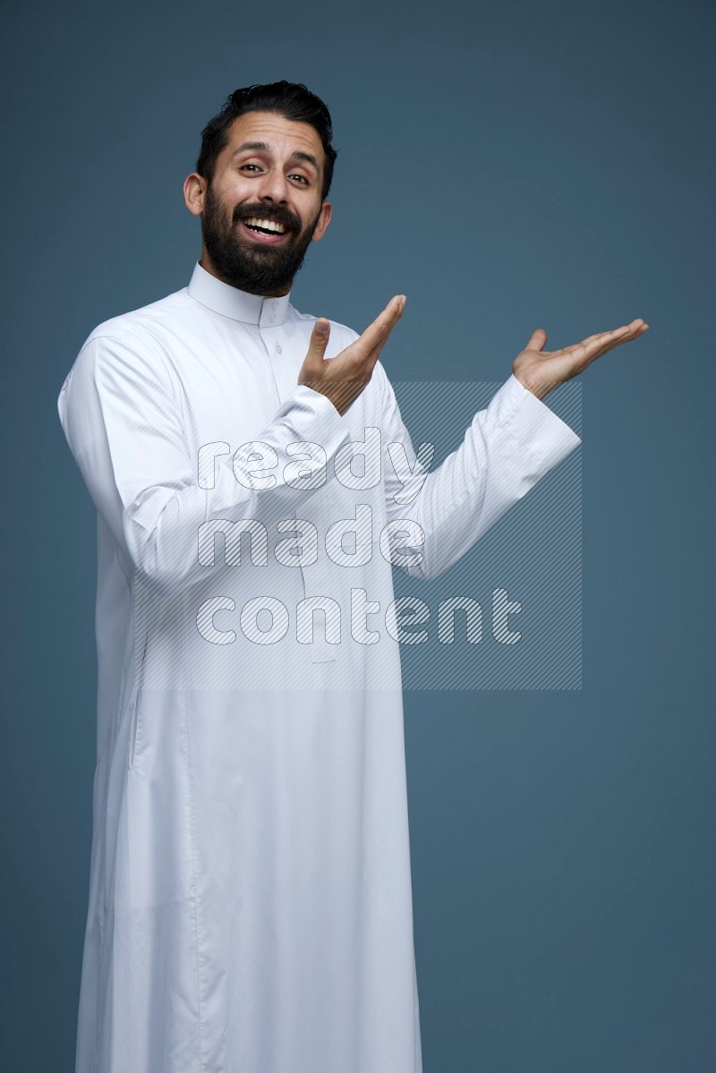 A man pointing in a blue background wearing Saudi Thob
