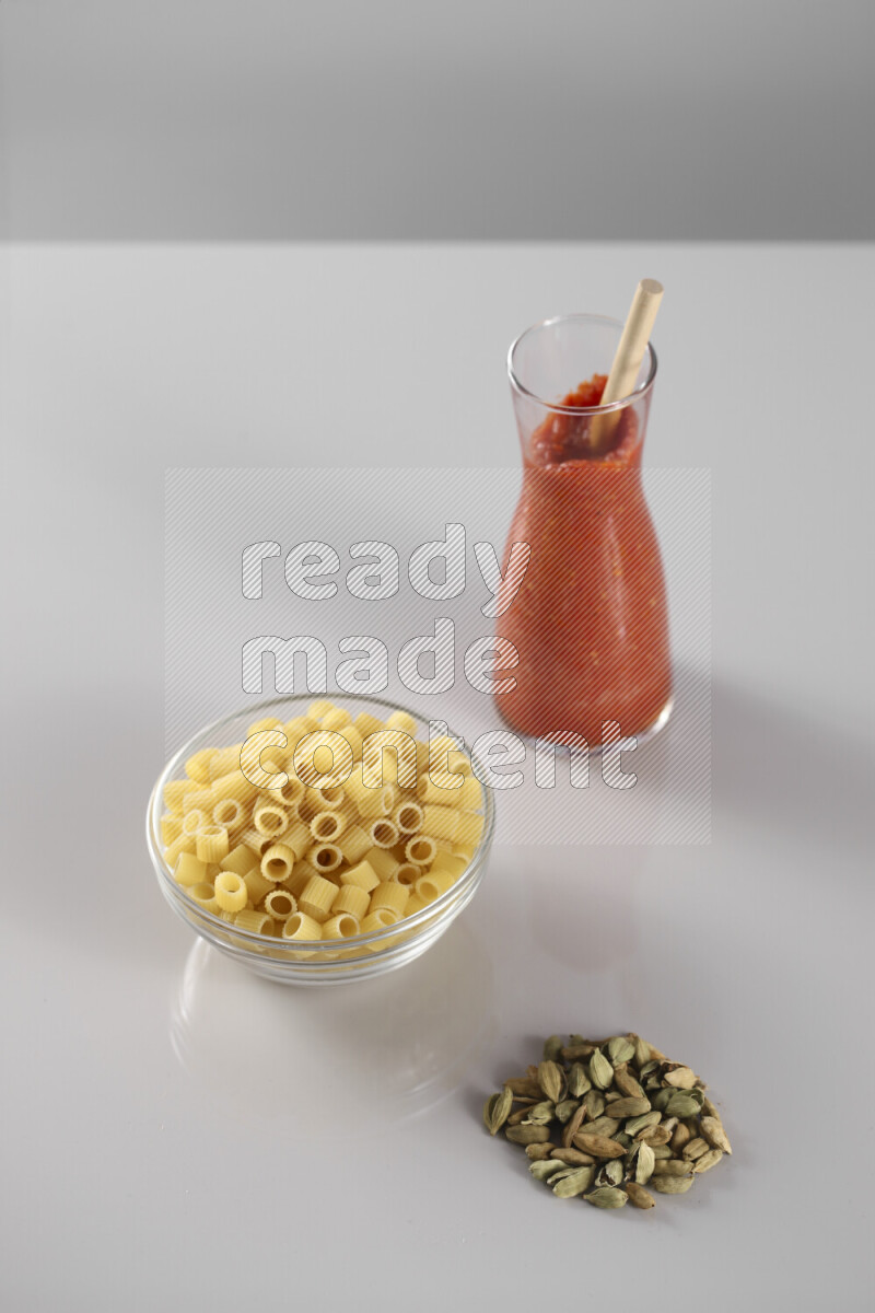 Raw pasta with tomatoe pasta with different ingredients such as cherry tomatoes, basil, garlic, bay laurel, cardamom, white pepper, black pepper, red chilis and wheat stalks on light grey background
