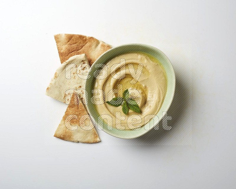 Hummus in a green plate garnished with mint on a white background