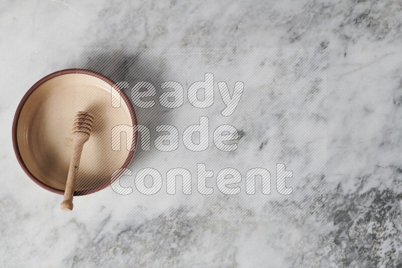 طبق فرن فخاري بيج مع ملعقة عسل خشبية بداخله على خلفية من الرخام الرمادي