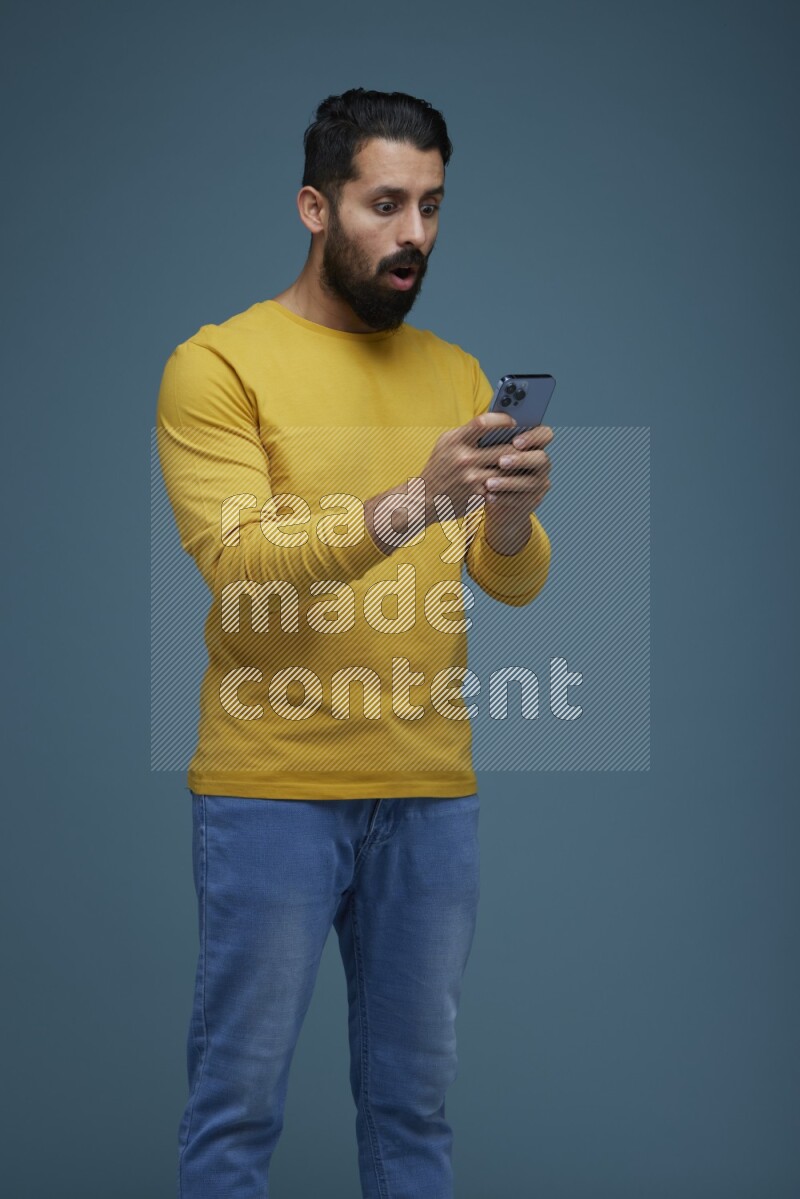 Man typing on his phone in a blue background wearing a yellow shirt