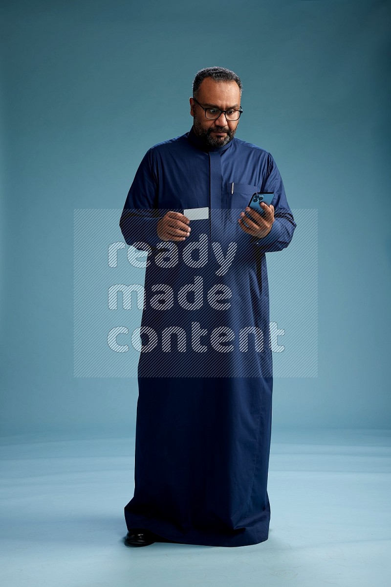 Saudi Man without shimag Standing holding ATM while talking on phone on blue background