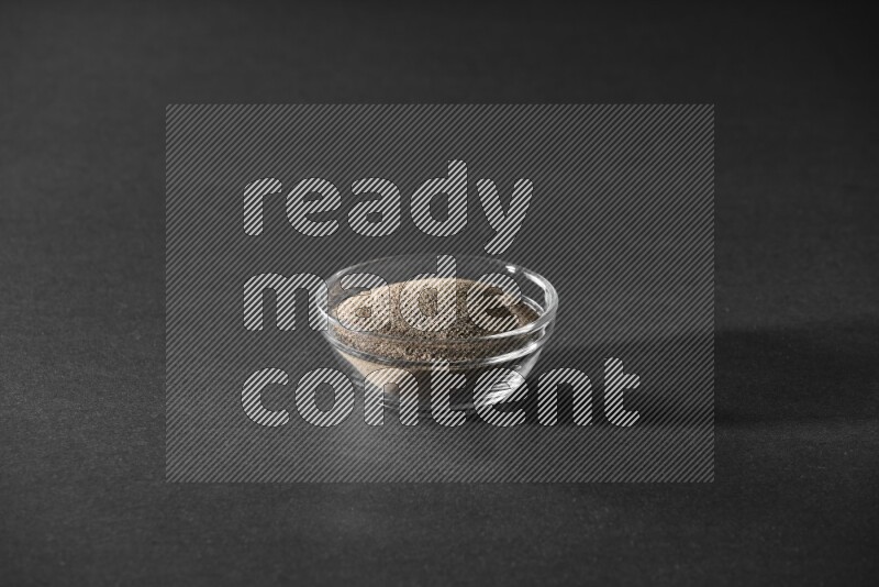 فلفل أسود مطحون في وعاء زجاجي علي خلفية سوداء