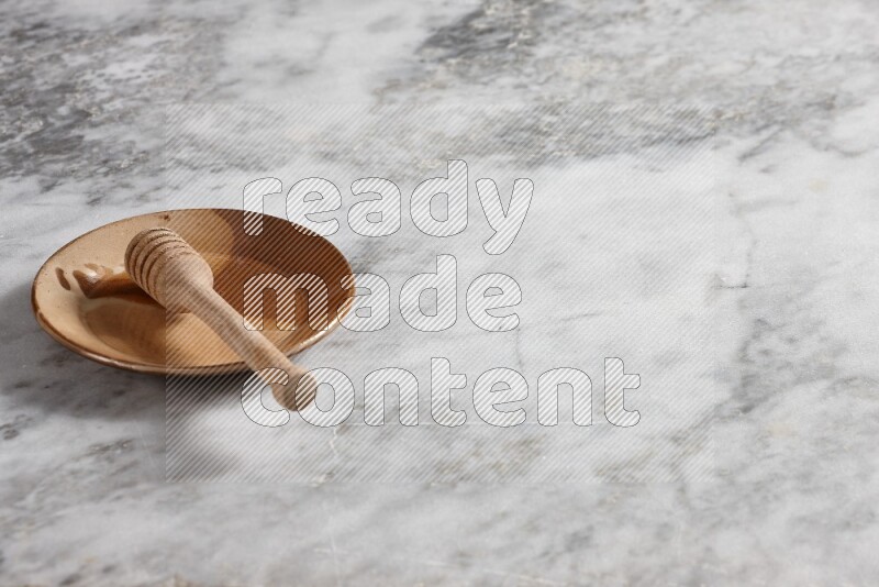 Multicolored pottery plate with wooden honey dipper in it on grey marble background