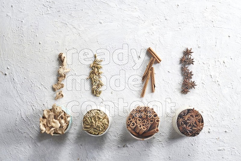 Cardamom, ginger, cinnamon sticks and star anise in 4 bowls on a textured white background