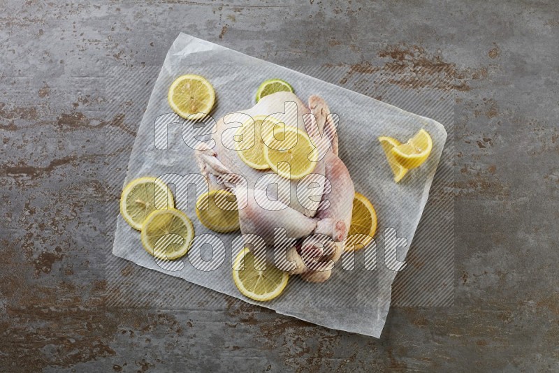 whole raw chicken on a parchment paper direct on a rustic grey background