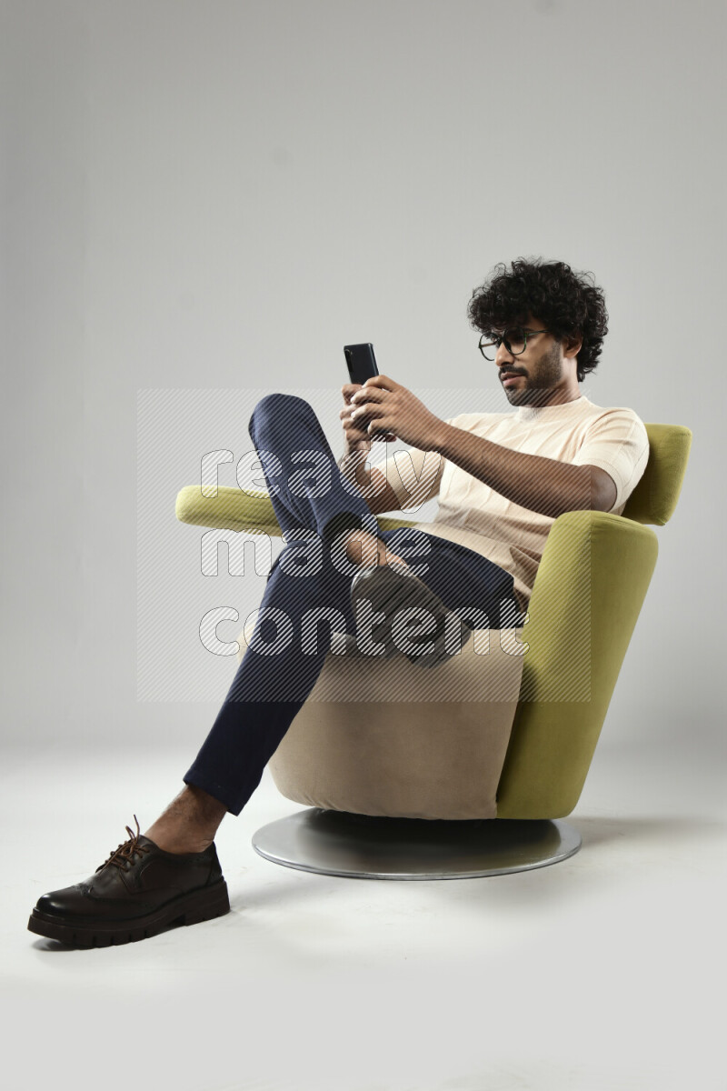 A man wearing casual sitting on a chair texting on the phone on white background