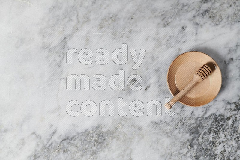 Beige Pottery Plate with wooden honey handle in it, on grey marble flooring, Top View
