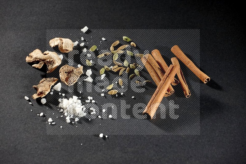 Ginger, salt, cardamom and cinnamon sticks on black flooring