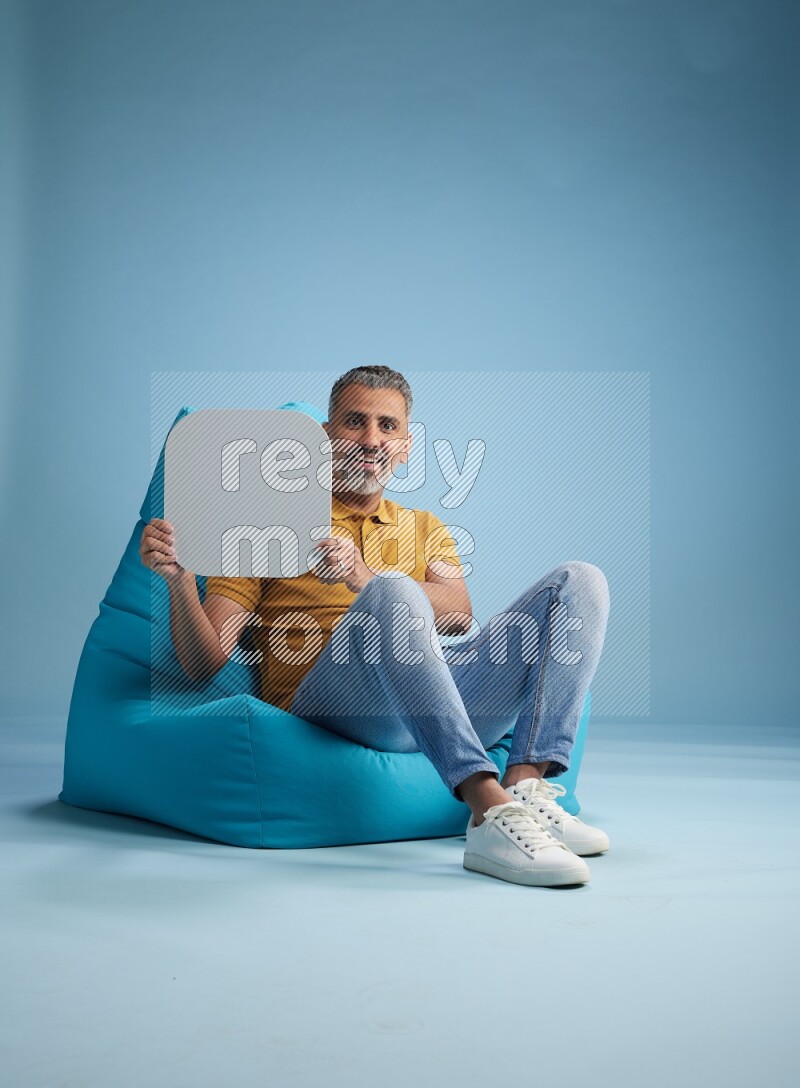 A man sitting on a blue beanbag and holding social media sign