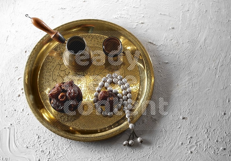 Dates in a metal bowl with coffee and prayer beads on a tray in a light setup