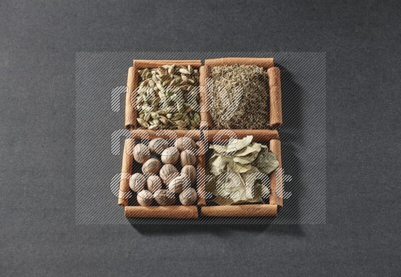 4 مربعات من عيدان القرفة ممتلئة بالكمون وحبوب الهيل وأوراق الغار وجوزة الطيب على أرضية سوداء