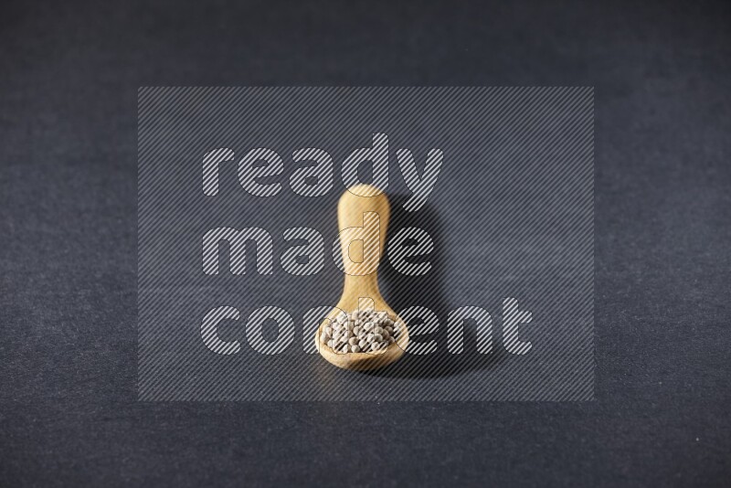 ملعقة خشبية مملوءة بحبات الفلفل الأبيض على أرضية سوداء