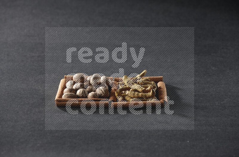 مربعان من أعواد القرفة ممتلئان بجوزة الطيب وأصابع الكركم علي خلفية سوداء